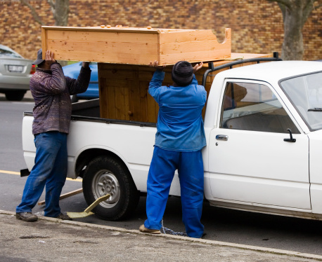 Workmen load wooden furniture on to a pick-up truck.