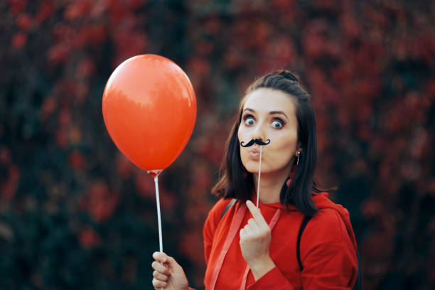 Woman Holding Paper Mustache Party Accessory and Red balloon Quirky girl holding a party accessory celebrating anniversary or festive carnival event women movember mustache facial hair stock pictures, royalty-free photos & images