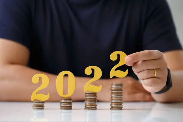 Photo of Man hands putting gold wooden number 2022 on stack of coins. tax payment, investment and banking.2022 New year saving money and financial planning concept.