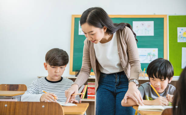 istock Pupil boy asking his teacher in classroom at elementary school. Student boy studying in primary school. Children writing notes in classroom. Education knowledge, successful teamwork concept banner 1341025624