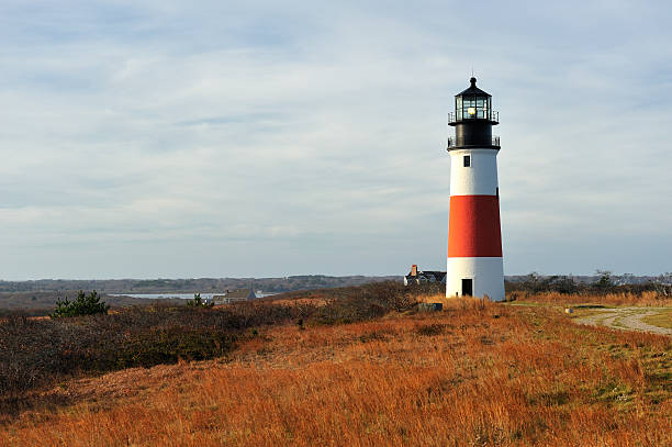 Sankaty Head Light Lighthouse, Nantucket, Massachusetts, USA Sankaty Head Light Lighthouse, Nantucket, Massachusetts, USA. Wide-angle view across the moors in autumn. Built in 1850, in 2007, the Sankaty Head Lighthouse was moved from the edge of an eroding bluff to its current location, 250 feet from the bluff's edge, near the fifth hole of the Sankaty Head Golf Course and overlooking the Nantucket moors. "Sankaty", from the Indian "sankoty", means highland. The 70 foot tall red and white brick lighthouse was built in 1850. It was the first lighthouse in Massachusetts with a Fresnel lens, which was replaced in 1950 with a rotating aerobeacon. The light was automated in 1965 but Coast Guard personnel occupied the station until 1992. sankaty stock pictures, royalty-free photos & images