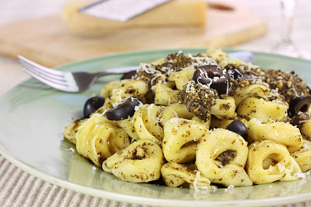 A hot plate of tortellini in pesto sauce with black olives