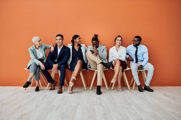 オレンジ色の背景に座っているビジネスマンのグループのショット - 人材採用 ストックフォトと画像