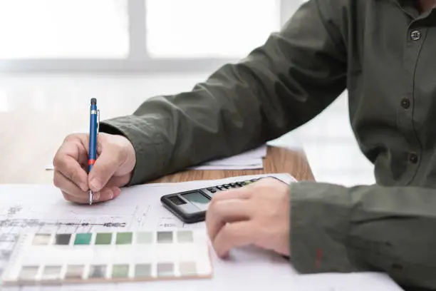 Photo of A man use pencil write in drawing in engineering work  with calculator paint chart and drawing on table