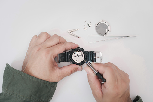 A man use pliers to clamp the digital watch battery remove and change in repairing broken wristwatches on white table