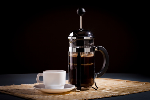 French press coffee maker and coffee cup studio lit on table with dark background