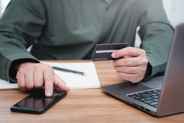 istock Businessman make online banking, making a payment or purchasing on the internet entering his credit card details on a smartphone and use laptop working on table 1341049854