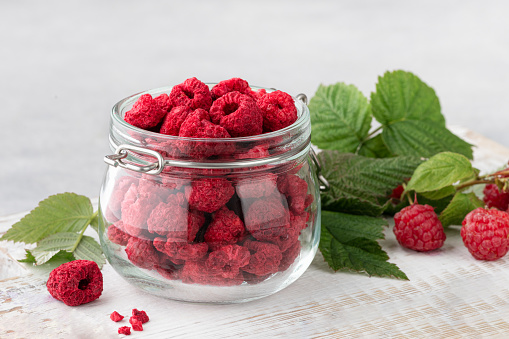 freeze-dried raspberries in a glass jar, fresh raspberries with leaves