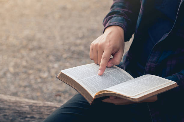 primo piano delle mani dell'uomo mentre legge la bibbia all'esterno. letture domenicali, educazione biblica. spiritualità e concetto di religione. - teologia foto e immagini stock