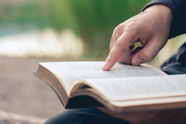 Close-up of man's hands while reading the Bible outside.Sunday readings, Bible education. spirituality and religion concept. stock photo