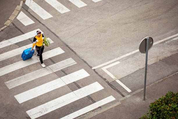 Adventurous female solo traveler, pushing her luggage, holding a plant, and listening to music, while walking on the street, in the direction she needs to go
