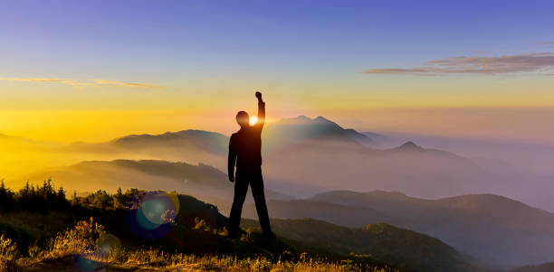 Man Silhouette lève la main lors d’une randonnée au sommet de la montagne au coucher du soleil. Silhouette de l’homme escalader le sommet de la colline de montagne au démarrage du spectacle du lever du soleil, se battre pour atteindre l’objectif,  - Photo