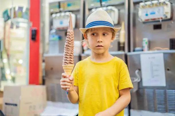 Photo of Little tourist boy eating 32 cm ice cream. 1 foot long ice cream. Long ice cream is a popular tourist attraction in Korea. Travel to Korea concept. Traveling with children concept