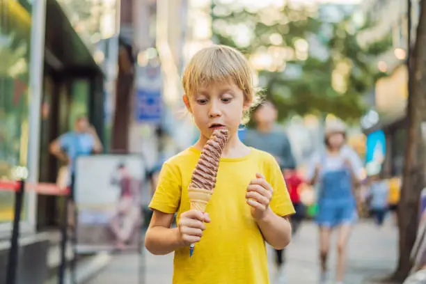 Photo of Little tourist boy eating 32 cm ice cream. 1 foot long ice cream. Long ice cream is a popular tourist attraction in Korea. Travel to Korea concept. Traveling with children concept