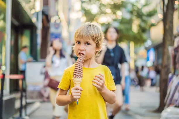 Photo of Little tourist boy eating 32 cm ice cream. 1 foot long ice cream. Long ice cream is a popular tourist attraction in Korea. Travel to Korea concept. Traveling with children concept