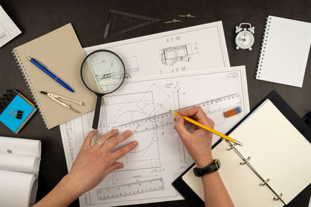 istock Mechanical drawing on sheets of paper. Hands on the table top view. Workflow of an architect, engineer. Write and draw. Ruler, pencil, notebook 1341073541
