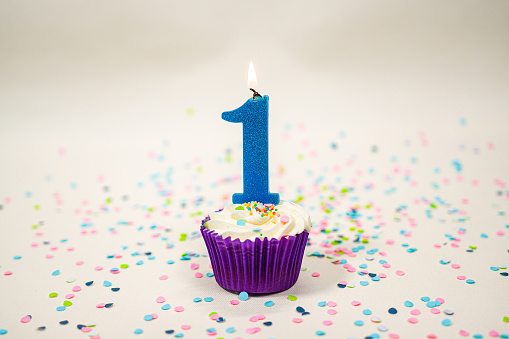 A cupcake with a lit candle on a canvas backdrop and round confetti to celebrate a first year in business.