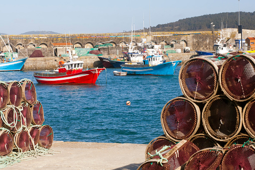 Old fishing boats, heaps of fishing net baskets and ropes on harbor dock.   Laxe,  Bergantiños, Costa da Morte, A Coruña province, Galicia, Spain.