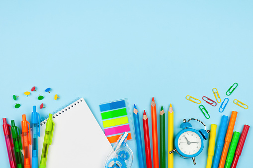 Variety of bright school supplies on blue background, copy space