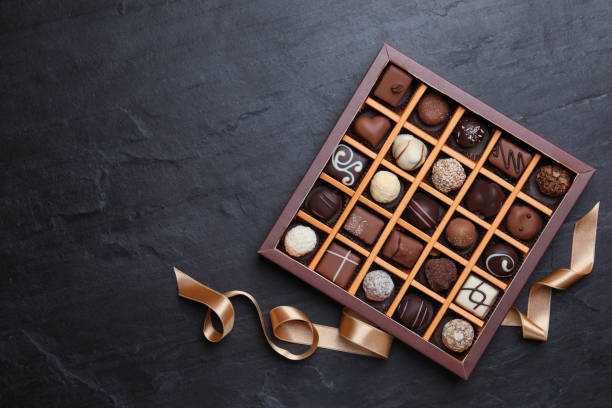 caixa com deliciosos doces de chocolate na mesa preta, flat lay. espaço para texto - chocolate truffle candy gourmet - fotografias e filmes do acervo