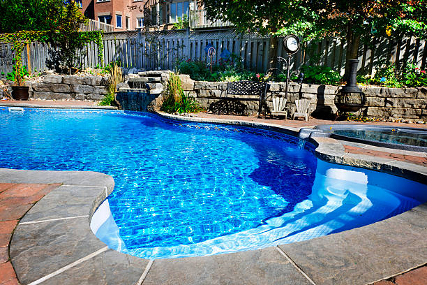 Swimming pool accented with a waterfall Residential inground swimming pool in backyard with waterfall and hot tub building feature stock pictures, royalty-free photos & images