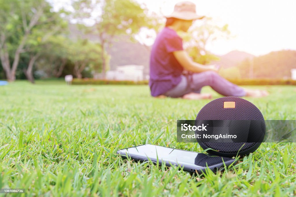 Close up smart phone Bluetooth speaker on the green lawn in Mountain"n garden with asia women Listening to music happily Speaker Stock Photo