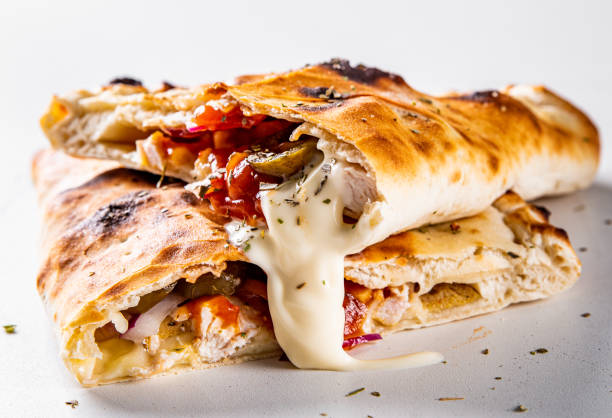 calzone pizza dobrado ao meio com carne, legumes e queijo em um fundo branco - pizza pastry crust oven meat - fotografias e filmes do acervo
