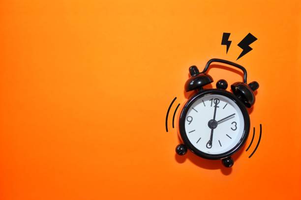 istock Black alarm clock on orange background 1341090347