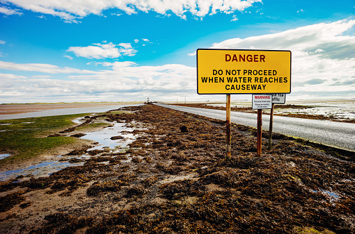 Danger sign at the entrance of the tidal causeway to Lindisfarne on the Holy Isle in the Northumberland region of England. Leica M10R 21mm Elmarit.
