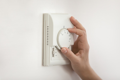 Climate control. Close up of young woman hand switch on temperature regulator on wall mounted panel turn controller to change thermostat position. Easy adjusting of modern heating system at smart home