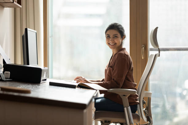 donna d'affari birazziale felice freelance siede al computer in un comodo posto di lavoro - sedia da ufficio foto e immagini stock