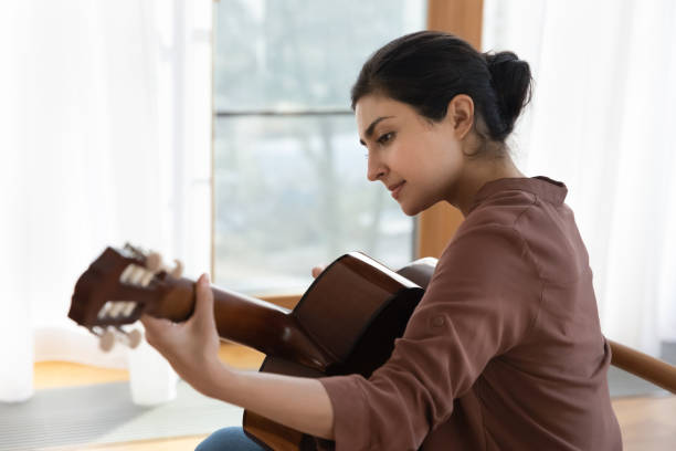 вдохновленная молодая индийская гитаристка держит гитару играть лирическую мелодию - lyrical стоковые фото и изображения