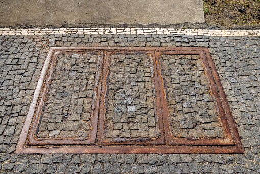 Hatch to technical installations with rust and cobblestones at the harbor in Ponta Delgada which is the main city on the Portuguese Azorean island San Miguel in the center of the North Atlantic Ocean