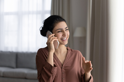 Phone talk. Positive young lady of indian ethnicity speak on telephone hold gadget at ear negotiate affairs. Pleasant hindu woman answer call on cell enjoy conversation with friend business partner