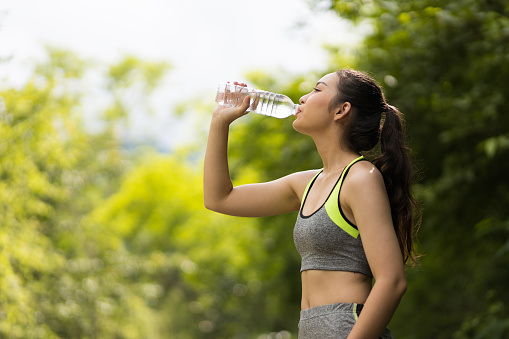 A thirsty Asian female athlete is drinking water after a workout.