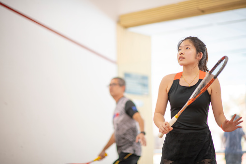 Asian squash coach father guiding teaching his daughter squash sport practicing together in squash court