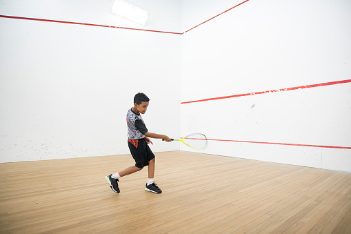 Asian malay boy squash player practicing alone in squash court during weekend routine