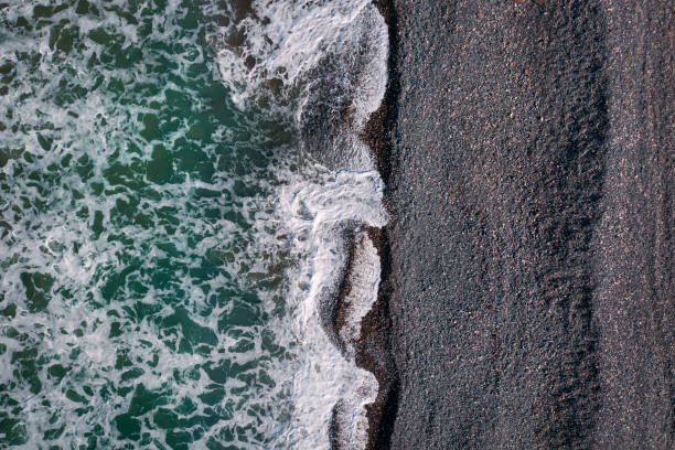 Green stormy waves with sea foam breaking on black sand beach, sea texture view from above Green stormy waves with sea foam breaking on black sand beach, sea texture view directly above black sand stock pictures, royalty-free photos & images