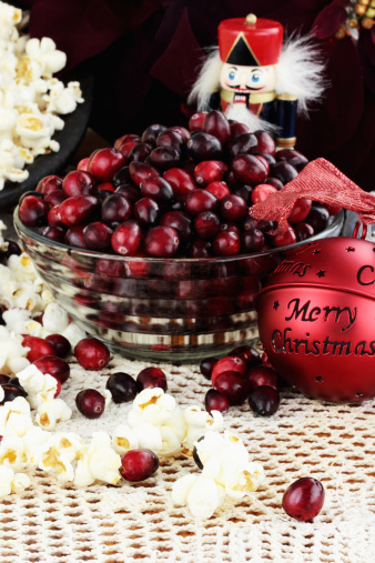 String of popcorn and cranberries with bowl of cranberries, popcorn, gift and ornaments in background.