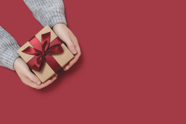istock Hands hold gift box tied with ribbon on a red background. 1341105013