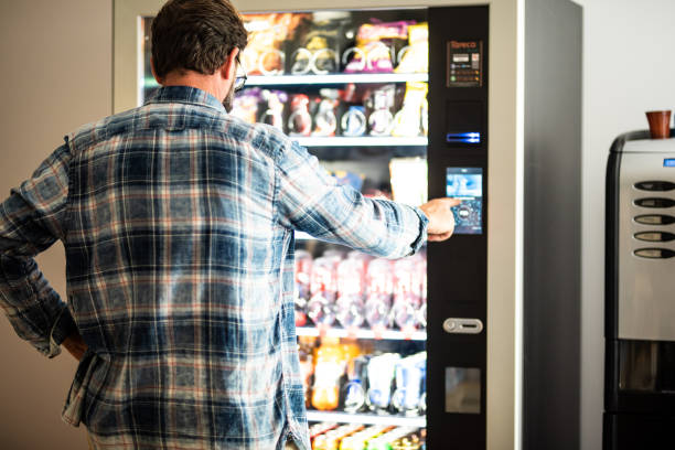 vista trasera del hombre usando la máquina expendedora - vending machine fotos fotografías e imágenes de stock