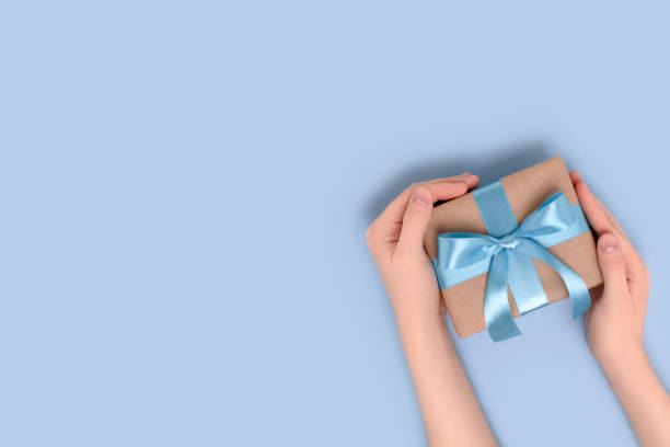 istock Female hands hold gift box on a blue background. 1341107524