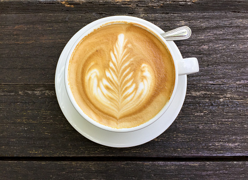 Top view of Latte coffee or cappuccino coffee in white cup with latte art on wooden table.