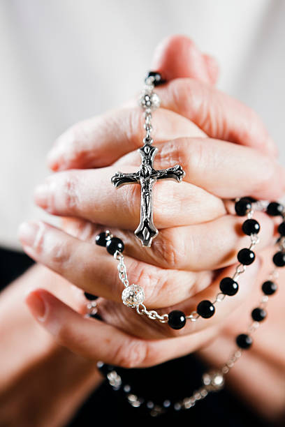 Elderly hands, clasped in prayer around a holy rosary Faith in action as an old woman holds her rosary and prays. Shot with Canon EOS 1Ds Mark III. nun praying cross human hand stock pictures, royalty-free photos & images