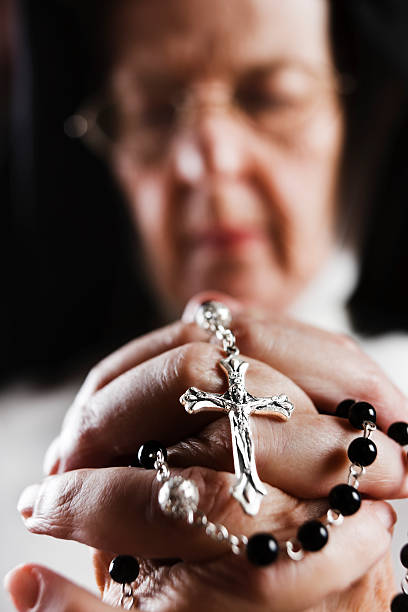 Faith in action: a nun prays Her rosary clasped in her praying hands, an old nun kneels, eyes closed. Focus is on the hands. Shot with Canon EOS 1Ds Mark III. nun praying cross human hand stock pictures, royalty-free photos & images