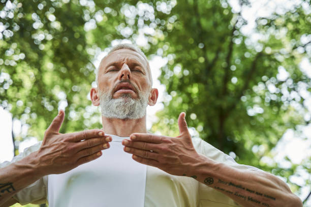 Ederly man keeping his eyes closed and doing breathing exercise while enjoying