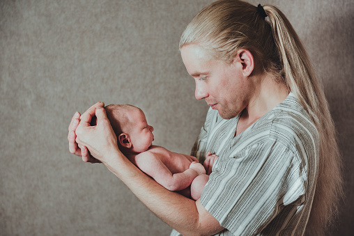 Close up portrait of young long haired father holding his newborn baby with copy space