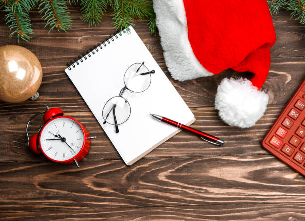 istock Christmas postcard santa hat, note book, glasses, golden ball, spruce branches, calculator, clock on a wooden background. 1341132060