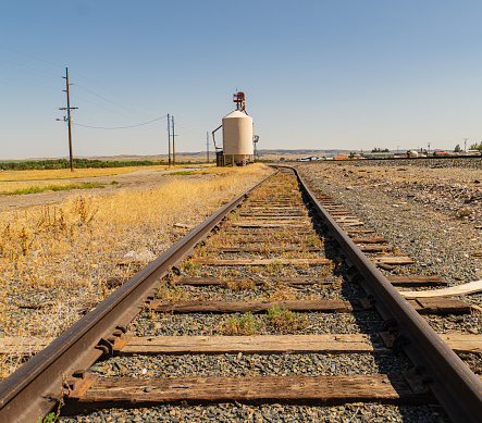 railroad tracts curve off to the left near a granary on the great flat plains in midwestern America