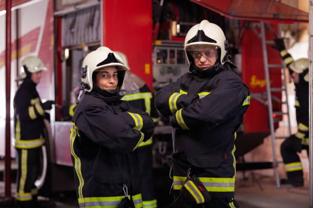 istock Two professional firefighters with uniforms and protective helmets posing infront of a firetruck. 1341134685